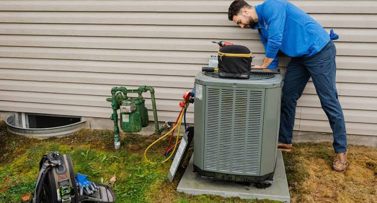 Technician in a blue shirt servicing a residential outdoor air conditioner
